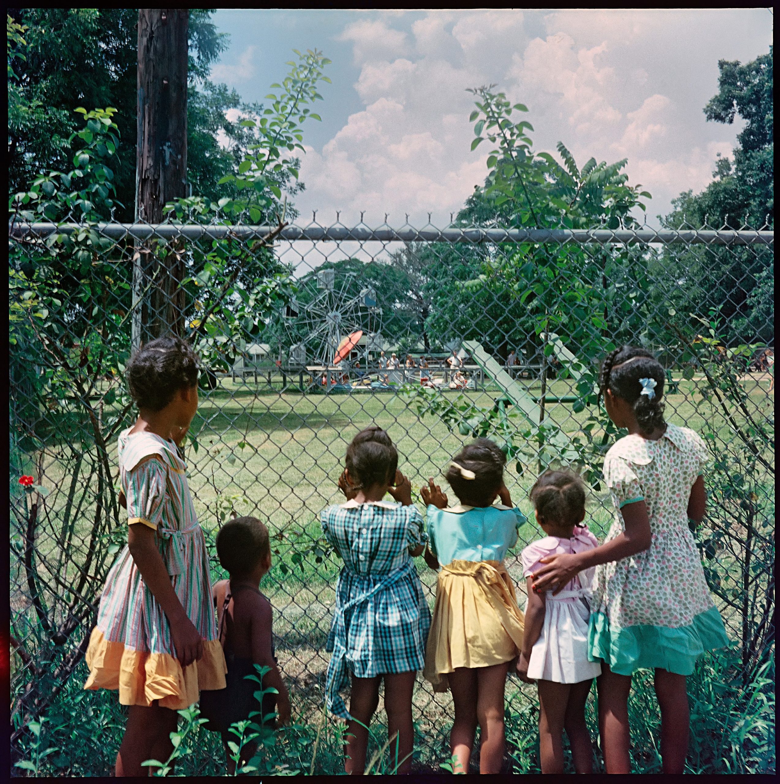 Five young girls and one boy look through a fence at a park in Mobile, Alabama in 1956