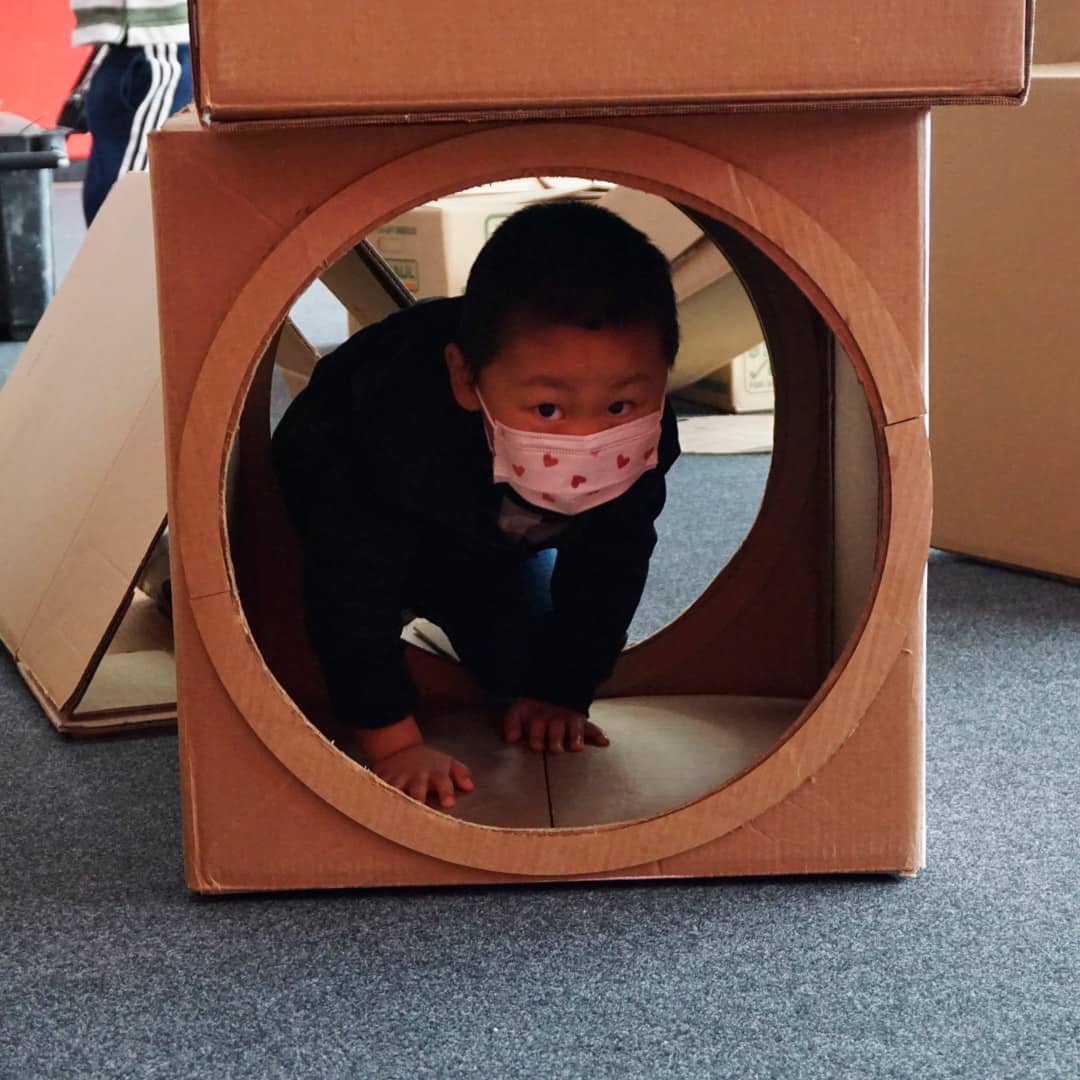A kid in a mask crawls through a cardboard box