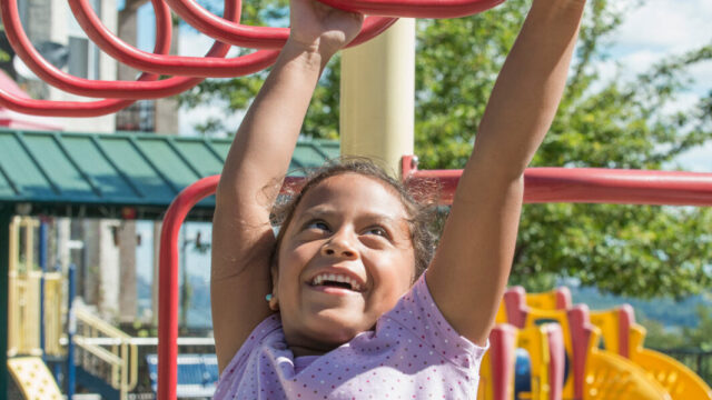 girl-hangs-from-playground-bars